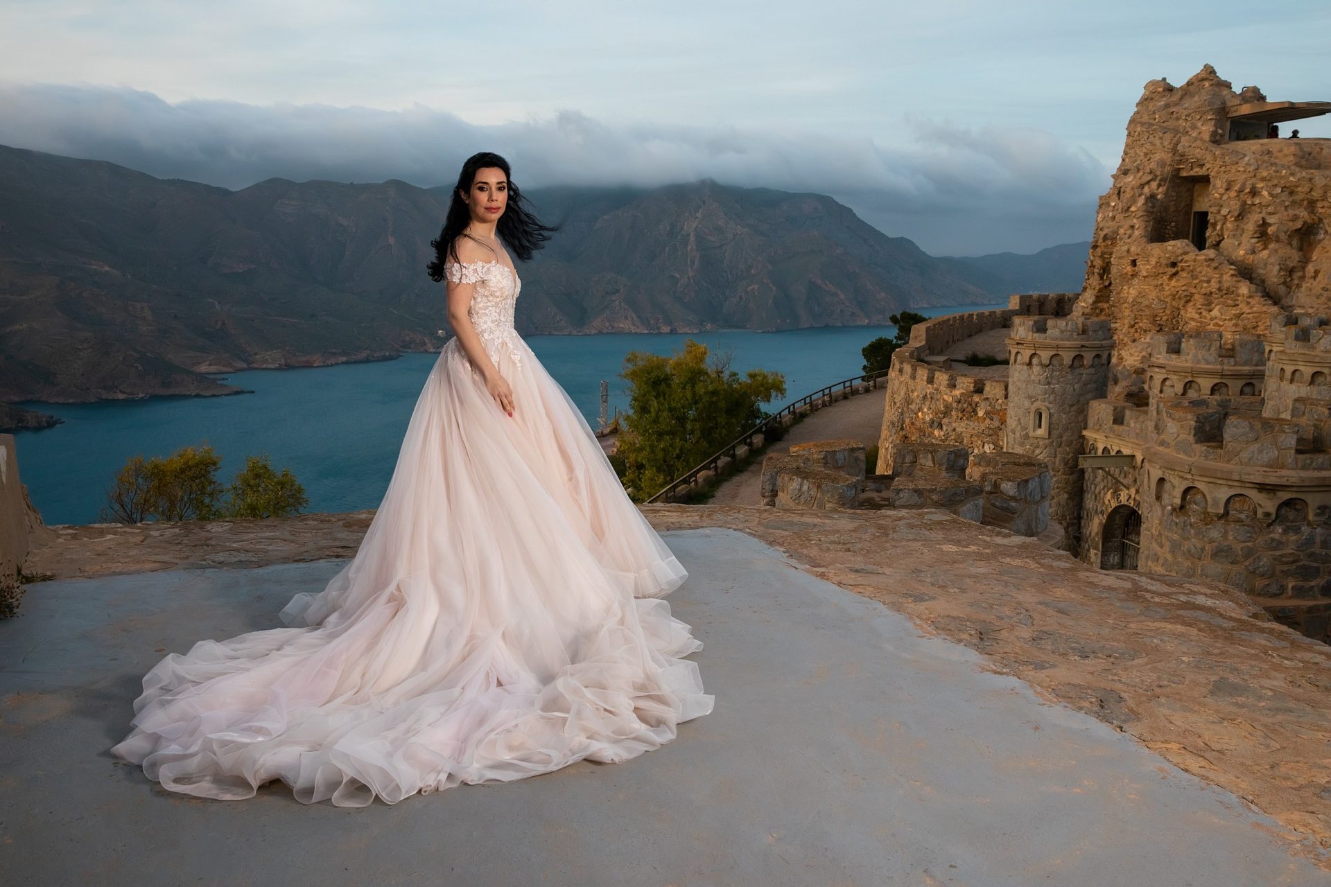 Novia con vestido de cola frente a un paisaje costero monumental