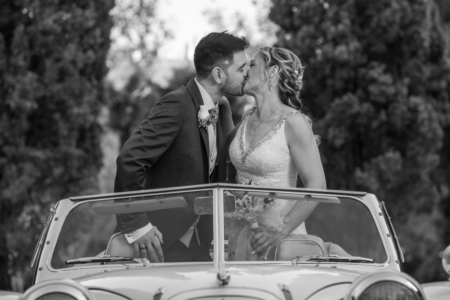 Novios besándose junto a un coche en blanco y negro