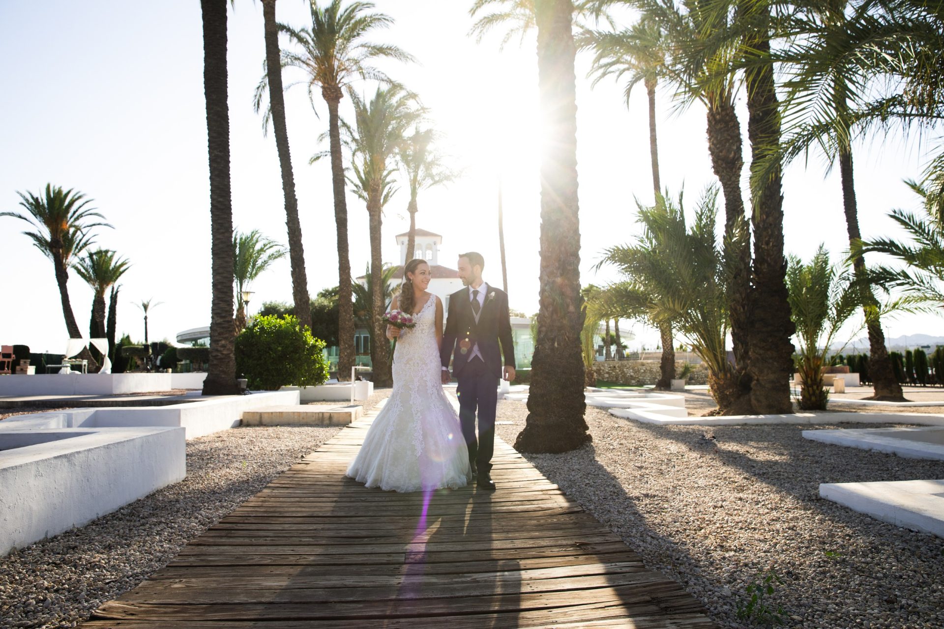 Pareja de recién casados caminando entre palmeras a contraluz
