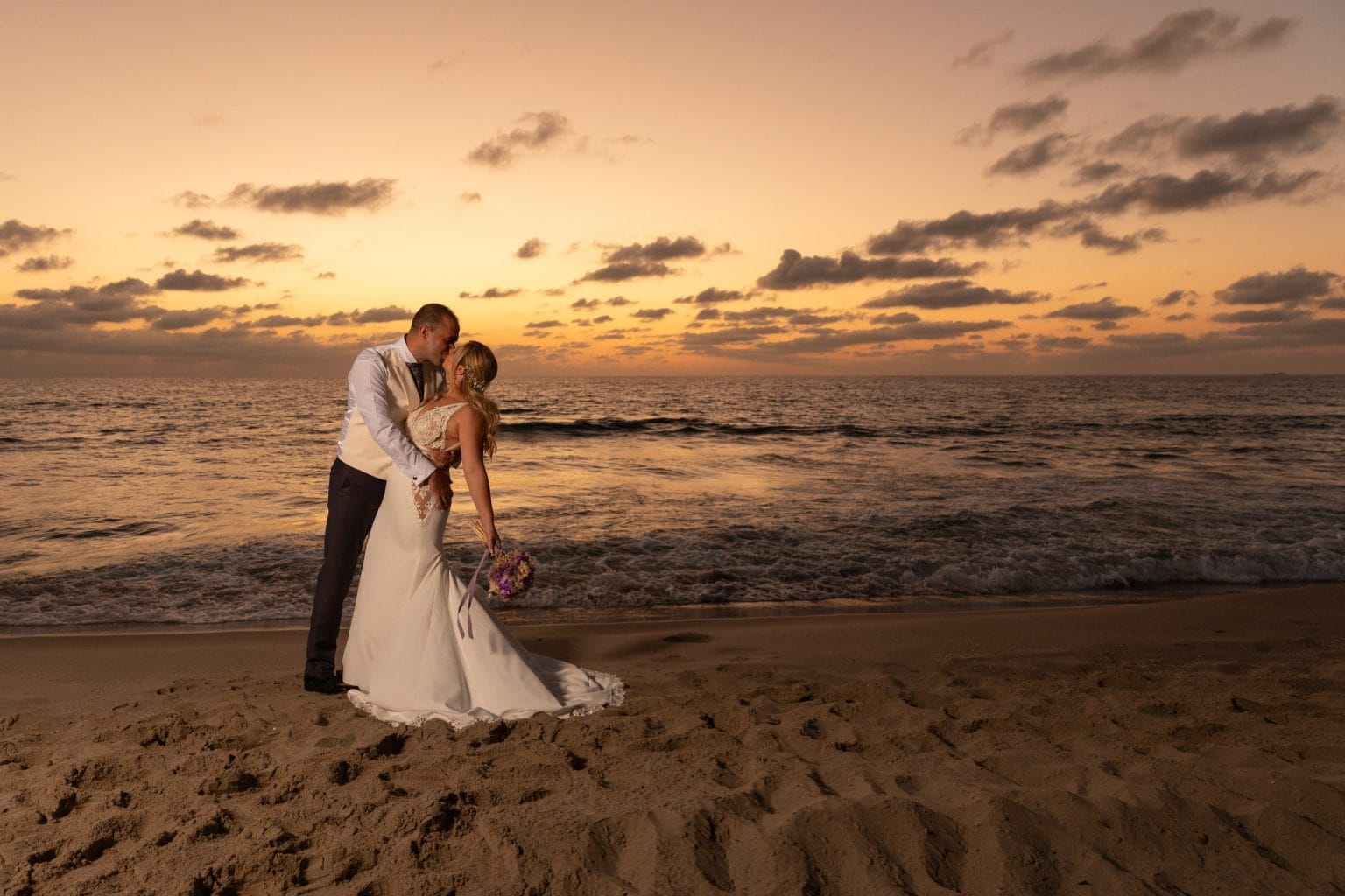 Pareja de recién casados abrazada frente al atardecer en la playa