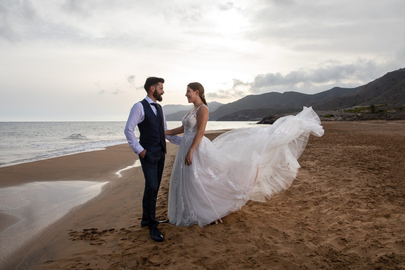 Pareja de recién casados en la costa con el velo movido por el viento