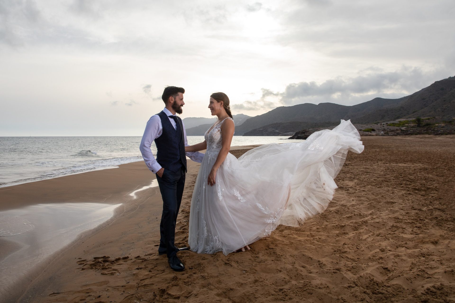 Pareja de recién casados en la costa con el velo movido por el viento